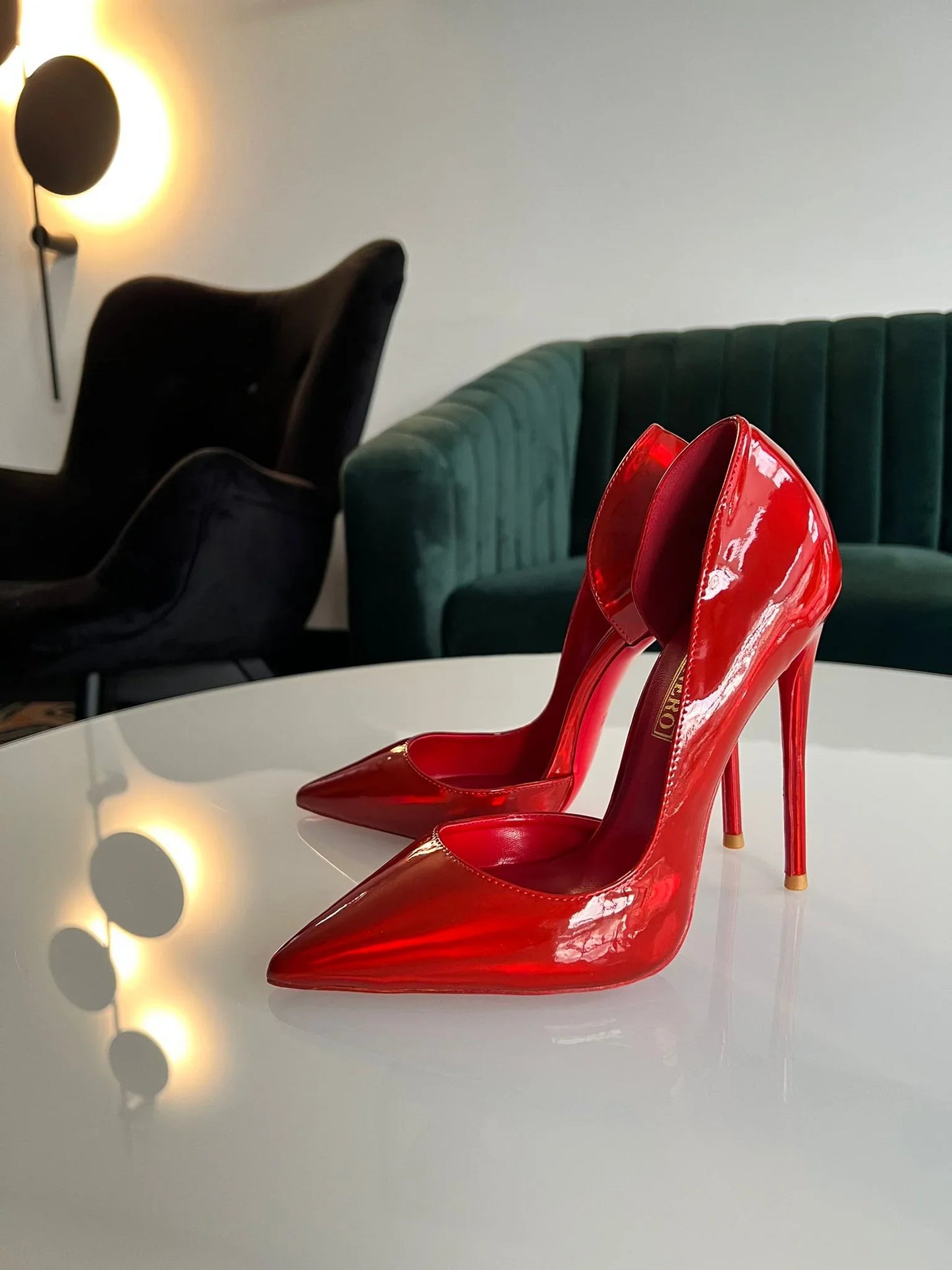 Shiny red stiletto high heels with pointed toes on a white table in a modern room