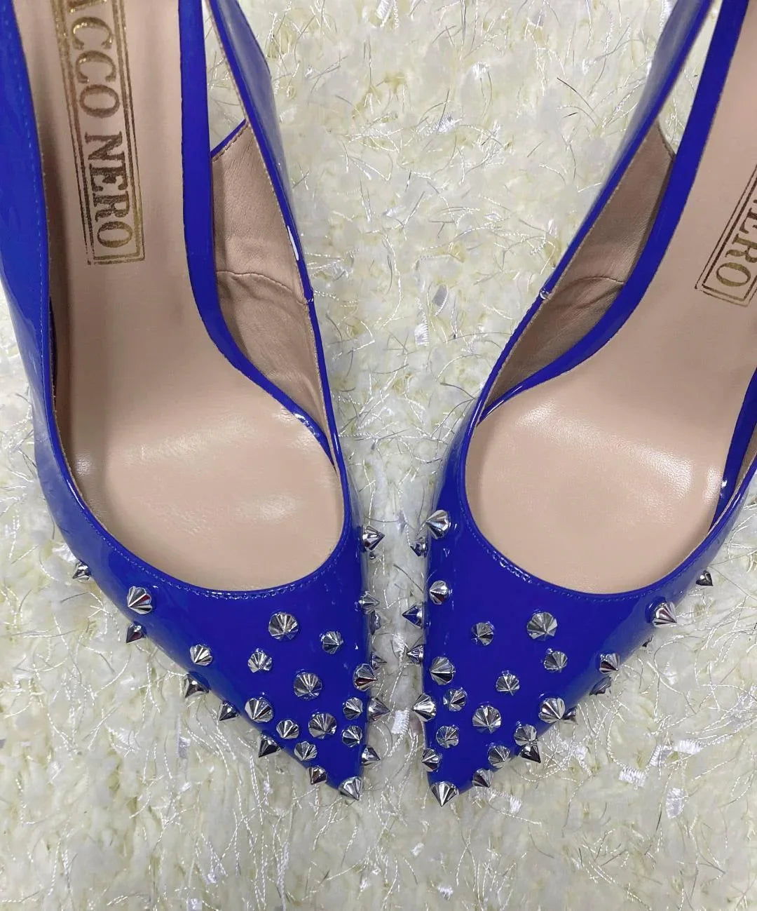 Blue pointed-toe high heels with silver studs on textured white background