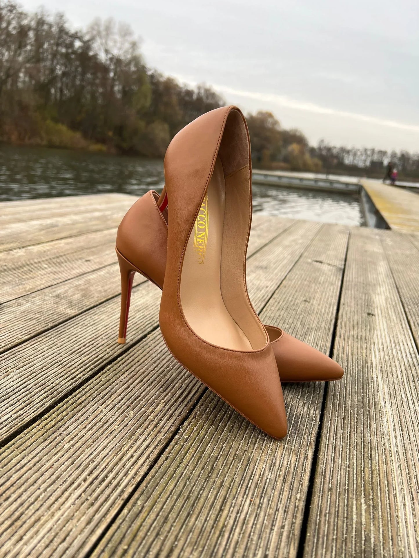 Brown leather high heels with pointed toe on wooden dock by water